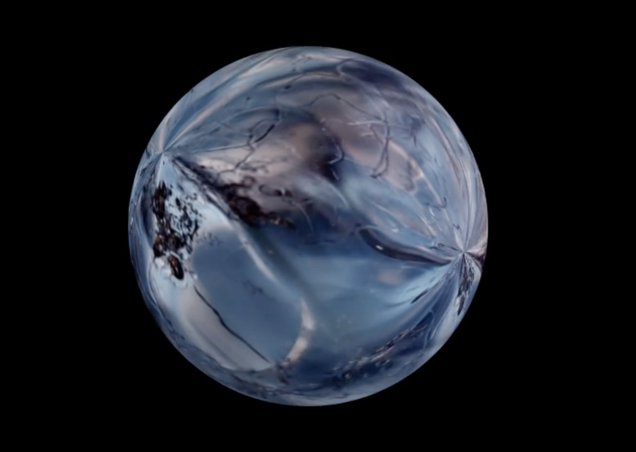 Image of an artwork by Ruth Le Gear. An iridescent orb floats on a black background. Blue, purple and mauve colours swirl across its glasslike surface. The image resembles that of a planet in deep space.