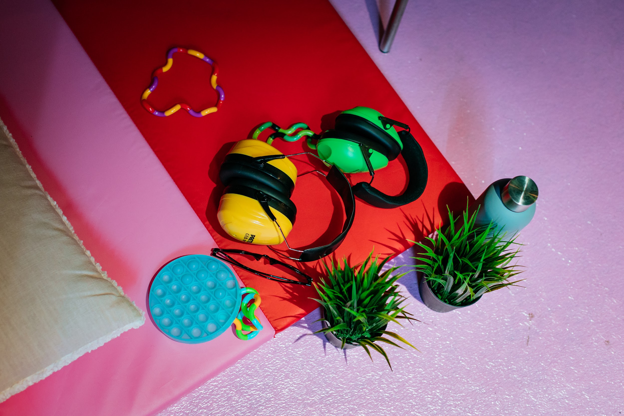 A collection of stim toys, ear defenders, a water bottle and plants, organised on a mat. Photo by Simon Lazewski.