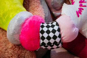 A close up shot of one of Rion Duffy Murphys soft sculptures. A snake like soft, wormlike cushion. Each ring of the snake a different pattern, a different texture.We see fluffy pink, we see black and white checker. In the background we soft, fluffy textures.