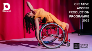 Artist Maryam Madani performs on the Disrupt stage. She is deep in a dance routine, arms outstretched, one to her face and one to the back of her wheelchair. She wears an orange dress, and her hair falls freely towards the ground. Behind her we see pink curtains and a purple floor.